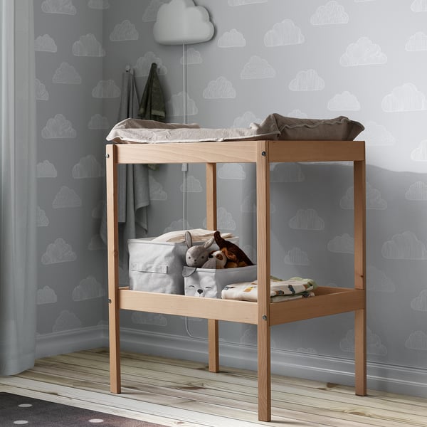 DRÖMSLOTT: small wooden changing table with changing pad, blankets, & soft toys. Wall has cloud patterns. Light grey, compact.