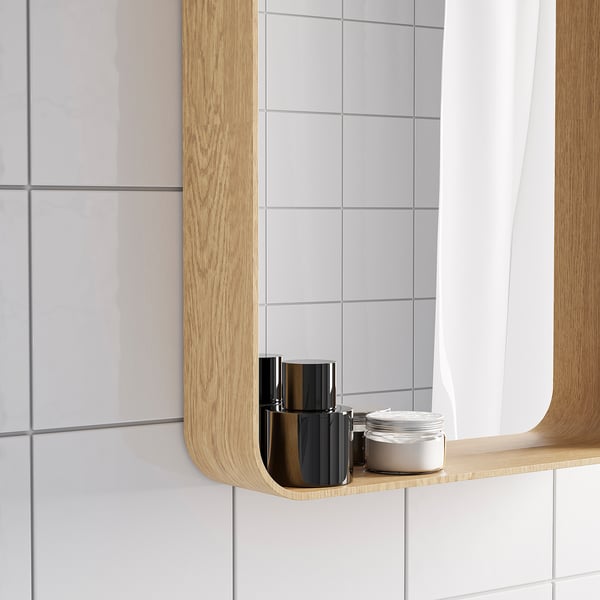 Wooden-framed mirror with shelf holds items, ideal for bathroom.