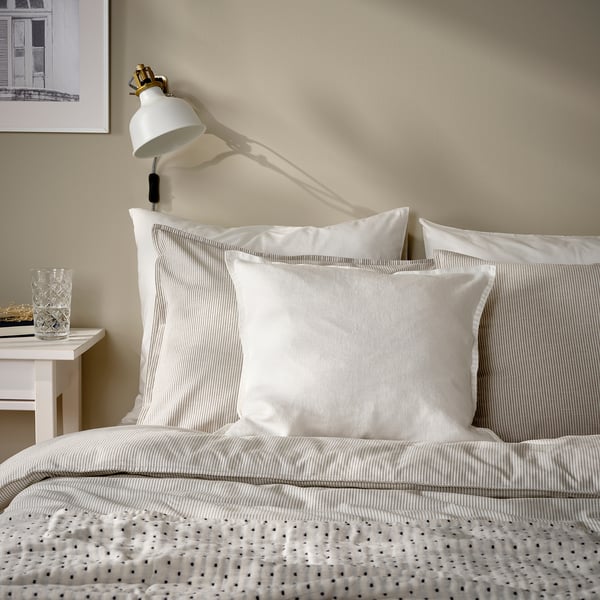 Neutral-toned bedroom with striped bedding, single white side table, and wall lamp.
