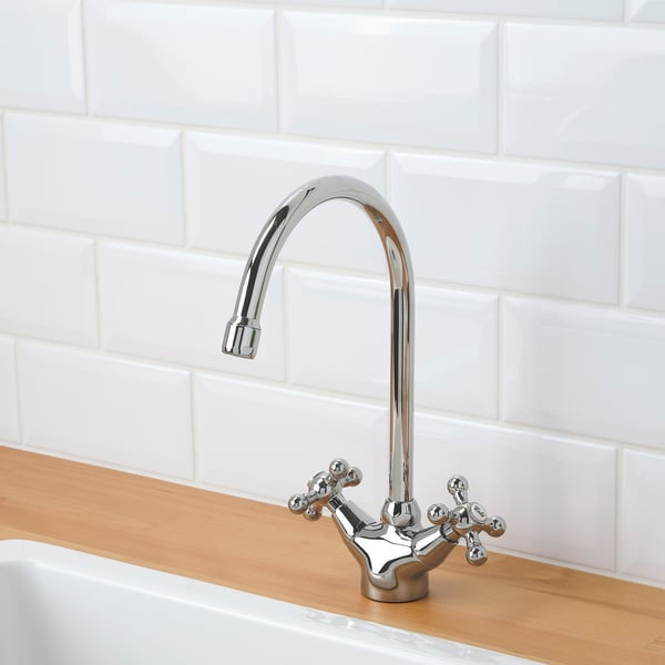 Modern chrome tap over wooden counter with white tiled wall, featuring high spout and dual handles.