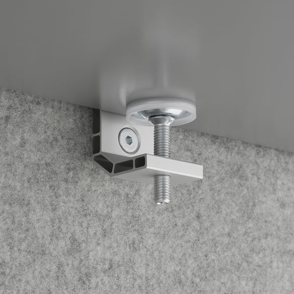 Metal clamp mounted on textured grey surface, securing a round metal piece with a threaded bolt.