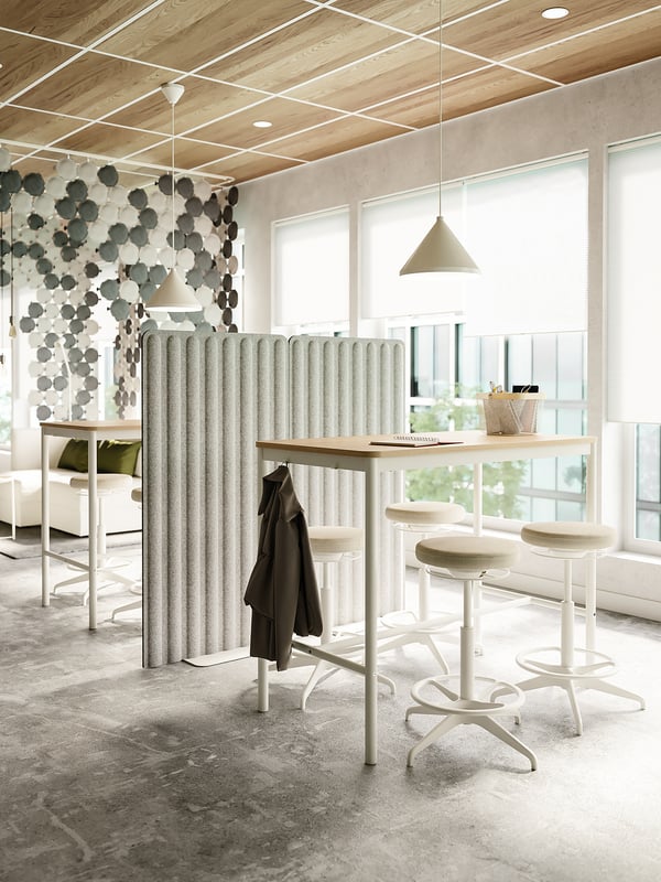 Modern office with stools, table, privacy screens, and natural light.