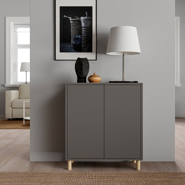 Modern grey EKET cabinet with door, lamp, and art. Grey cabinet has wooden legs, a table lamp, and a framed picture atop it.