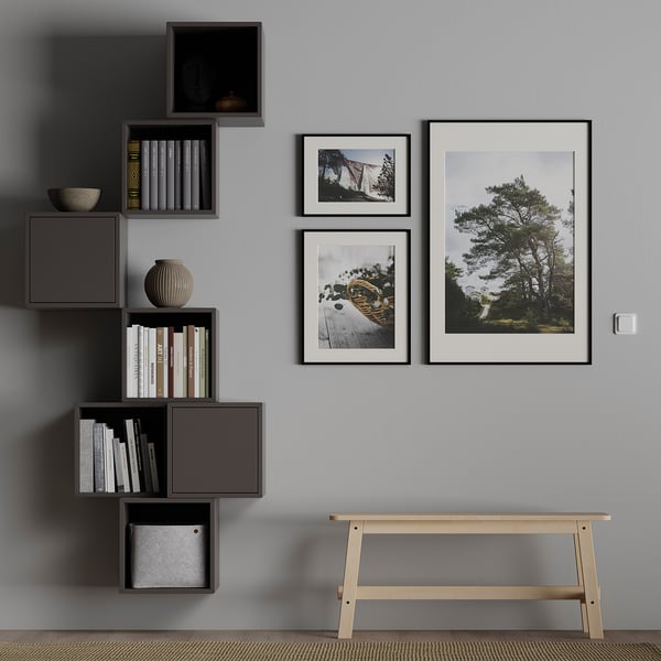 Modern room with modular grey wall shelves holding white and black books. Framed nature photos and a wooden bench.