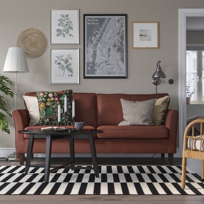 Cosy living room with large brown EKHOLMA sofa, black coffee table, striped rug, rattan chair, and wall art. Sofa cushions, candles, and lamps.