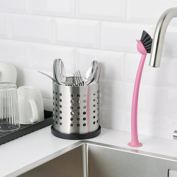 Kitchen scene with stainless cutlery organiser on counter and pink brush beside sink.