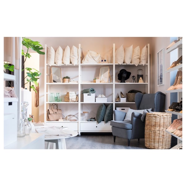 Modern living space featuring ELVARLI storage system with white shelves, grey chair, various pillows, and baskets.