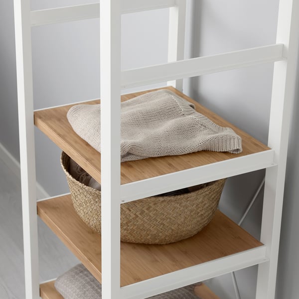 White metal shelving unit with wooden shelves. Top shelf holds folded beige blanket. Bottom shelf holds large woven basket.