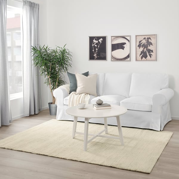 A minimalist living room with a beige ENGELSBORG rug, white sofa, coffee table, and green plant.