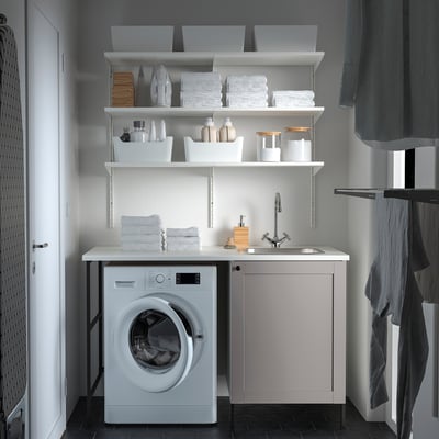 Modern, compact laundry setup with white ENHET counter, sink, and washing machine. Grey and white accents, organised storage.