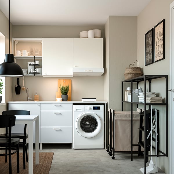Modern minimalist kitchen with white cabinets, black chairs, washing machine, and laundry bag, well-organized with shelves and hooks.