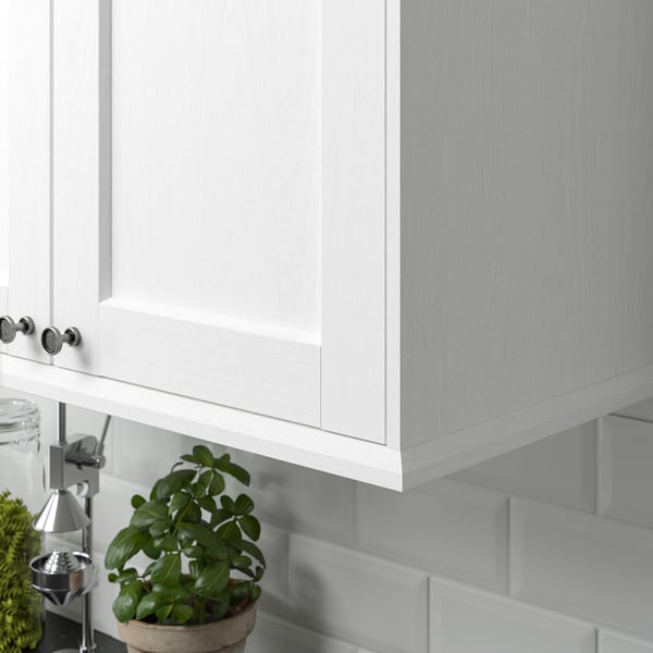 White kitchen cabinets with a subtle wood grain texture, light grey tiled backsplash, and a potted plant on the counter.