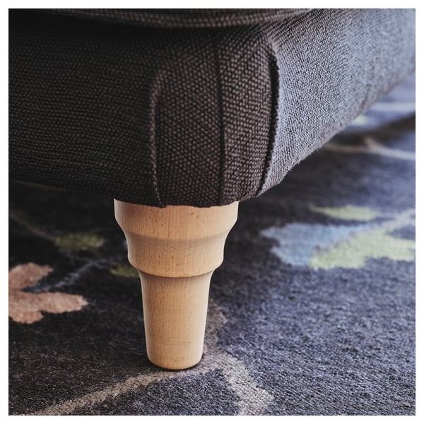 Close-up of a wooden leg with visible grain, supporting a dark fabric item on a patterned rug.