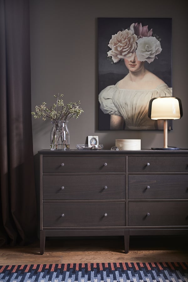 Elegant bedroom scene with dark dresser, floral art, and glass lamp.