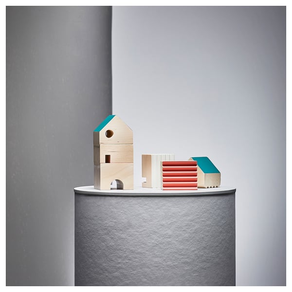 Three colourful wooden blocks, resembling wooden blocks, including a birdhouse, lined up on a table.