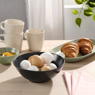 Breakfast table set with bowls, croissants, mugs, and napkins.