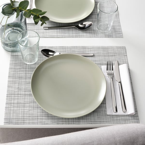 Two place settings with plates, glasses, cutlery, and folded napkins on woven placemats, ready for dining.