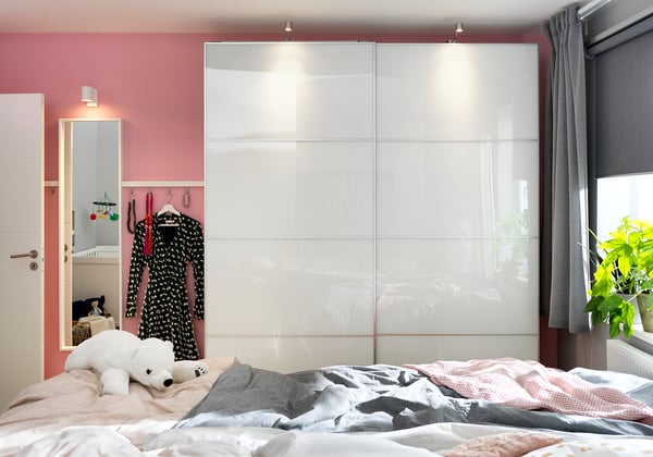 Bedroom with FÄRVIK white glass wardrobe, pink walls, grey curtains, and unmade bed featuring a teddy bear.
