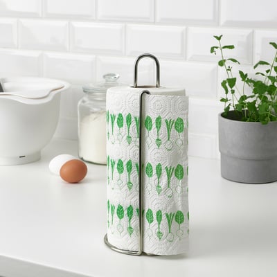 Metal holder with two-ply kitchen towels, displaying a green veggie pattern, resting on a white countertop.