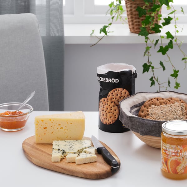 Wooden cutting board with cheese and knife; honey jar, crackers, jam, and plant.