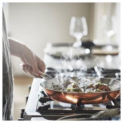 Copper FINMAT frying pan on stove, stainless handles, steam rising.