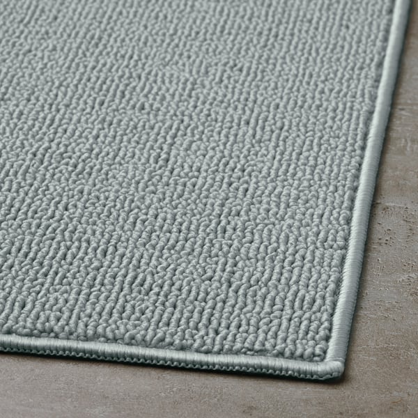 Light grey bath mat with a textured, looped fabric surface and a smooth border, displayed on a flat surface.