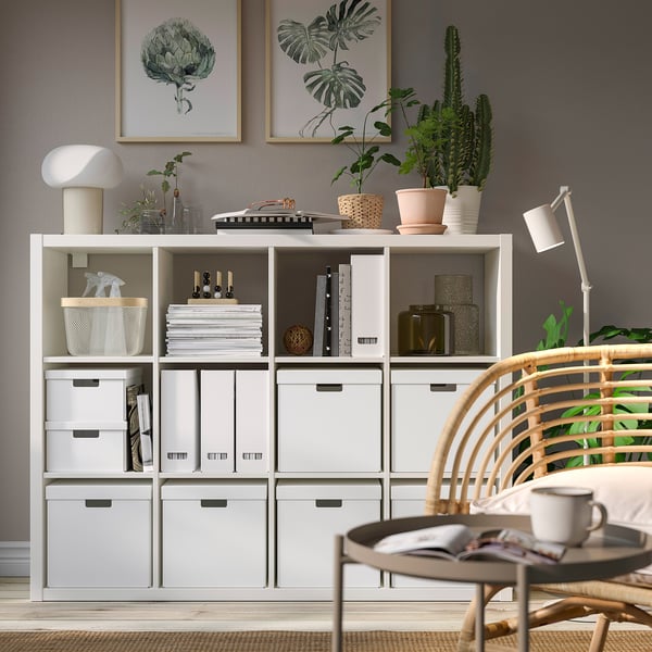 Shelf with FJÄDERHARV boxes, plants, decor, and office supplies. Nearby wicker chair with cup and magazine.