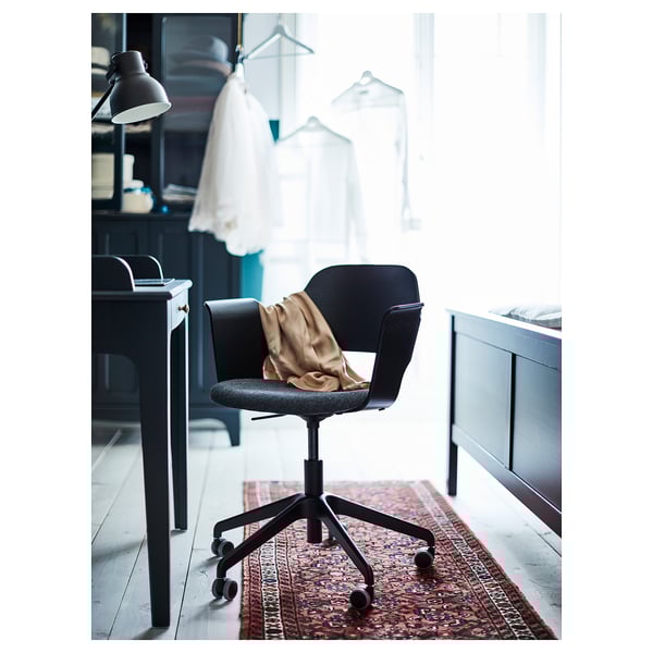 Black office chair, FJÄLLBERGET, with height adjust and wheels, covered in fabric, on a red rug near a desk.