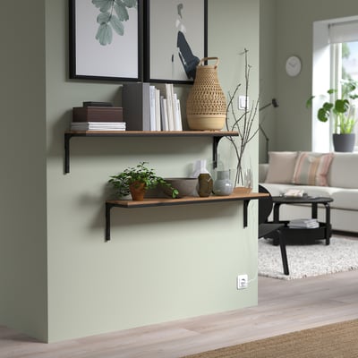 Modern living room with FJÄLLBO rustic wall shelves. Metal and wood design holds books, vases, plants. Light green wall, light-colored floor.