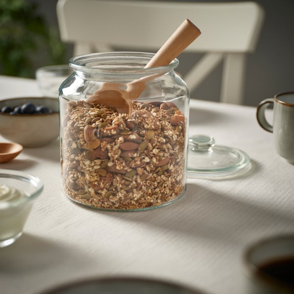 Jar of nuts & seeds with spoon on table.