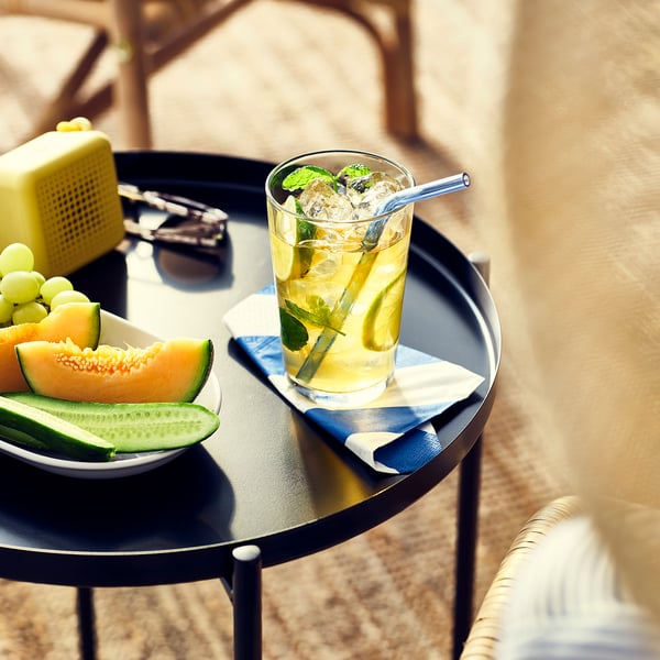 Glass of iced tea with mint on a table, next to plate of sliced melon and grapes.