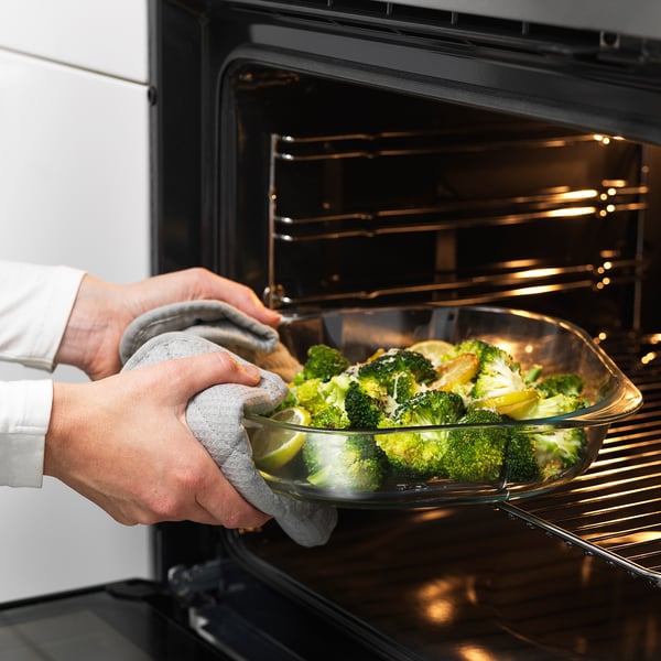Person placing glass dish with broccoli into oven. Handles allow for easy lifting.