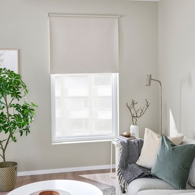Modern room: large window with beige FÖNSTERBLAD blind, grey sofa, plant, frame, lamp, cozy decor.