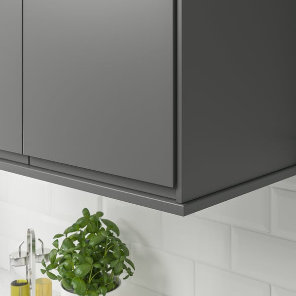 Grey kitchen cabinets with a white tiled backsplash. Under the cabinets, theres a plant and oil bottles.