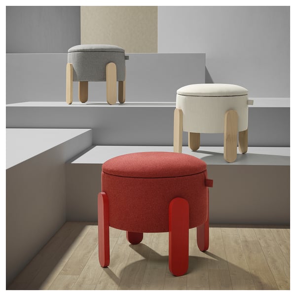 Three round, cushioned stools in red, gray, and beige, each with four wooden legs, arranged on a wooden floor, set against a gray wall.