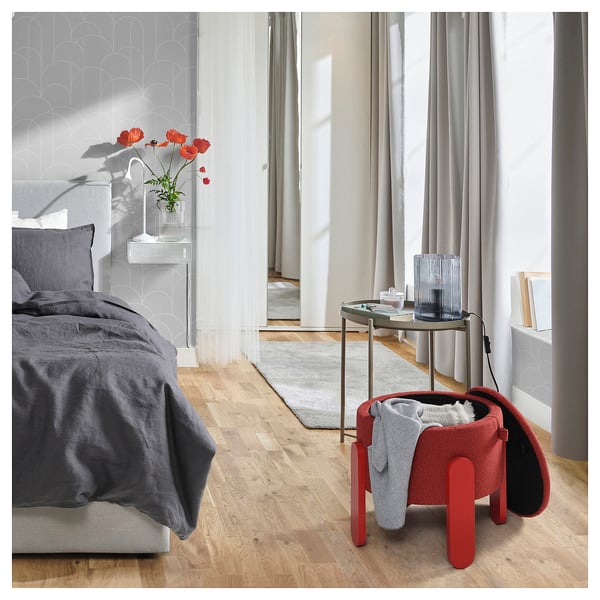 Red ottoman in cosy bedroom with grey bed, side table with flowers.