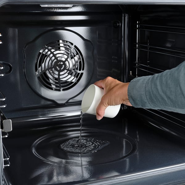 Person pouring water into an oven, likely for cleaning or steam function.