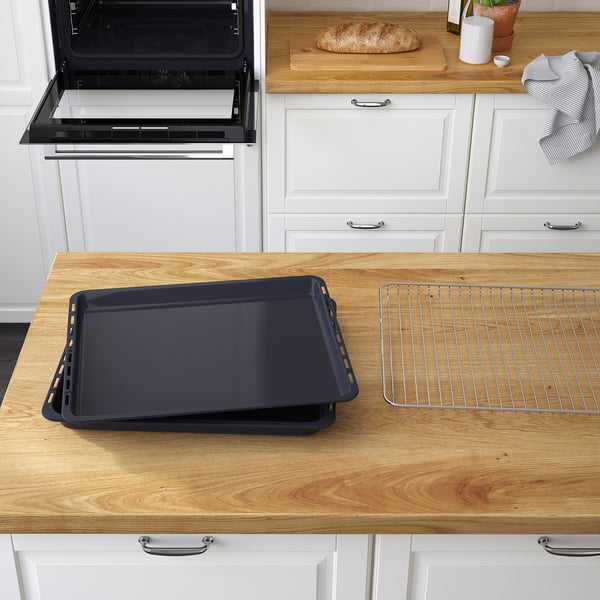 A kitchen with a black oven, dark baking tray, and cooling rack on wooden counter.
