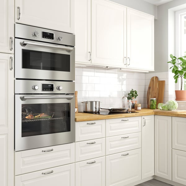 A modern kitchen with FORNEBY stainless steel built-in oven and microwave. White cabinets surround it, with a wooden countertop and tiled backsplash.