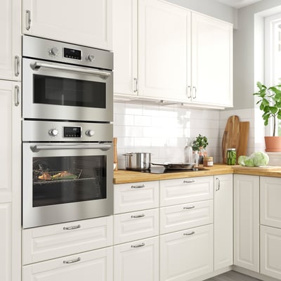 A modern kitchen with FORNEBY stainless steel built-in oven and microwave. White cabinets surround it, with a wooden countertop and tiled backsplash.