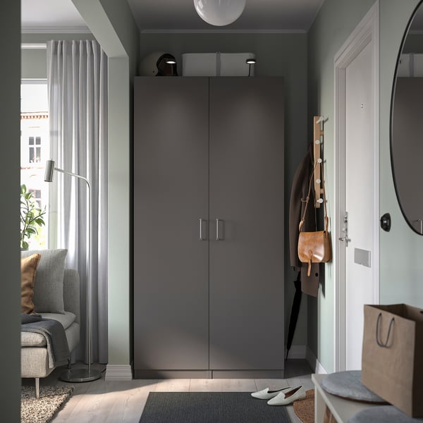 Modern entryway with dark grey pax wardrobe, white door, hanging coats, and grey decor.