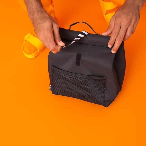 Person holding little black lunch bag with white stripes against orange background.