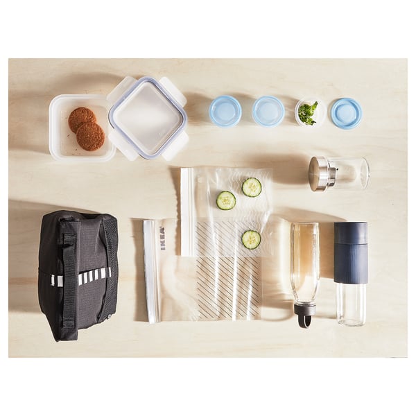 Image displays a black insulated lunch bag among various food containers, cutlery, and jars on a wooden table.