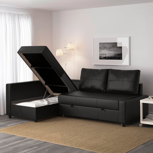 Black convertible sofa bed with open storage ottoman, showing mattress storage. Modern living room setting with art and lamps.