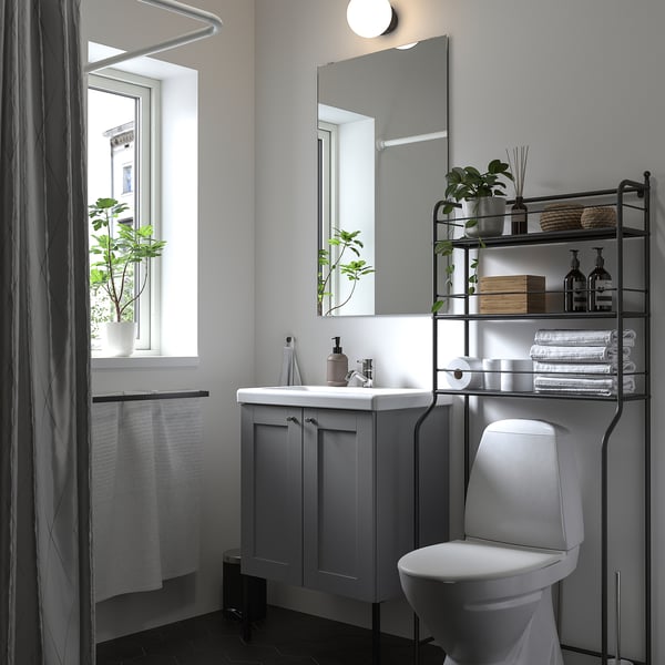 Modern bathroom with grey & white decor. Over-toilet, black wire shelves hold towels & plants. White toilet below.