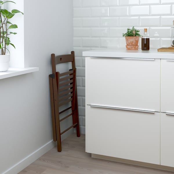 Wooden folding chair leans against white cabinets, designed for compact storage and easy access.