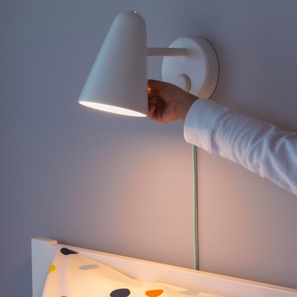 A person adjusting a dimmable wall lamp; warm, soft light illuminates nearby area.