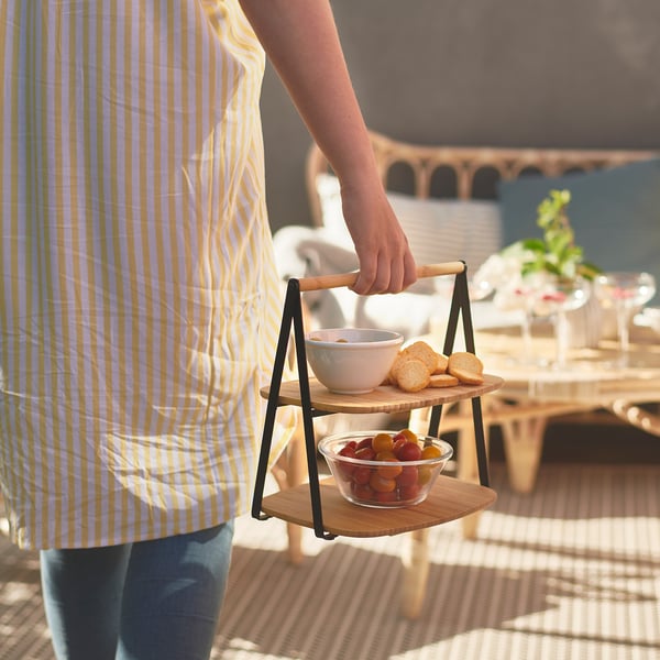 Person holding multi-level bamboo serving tray with snacks in yellow striped apron.