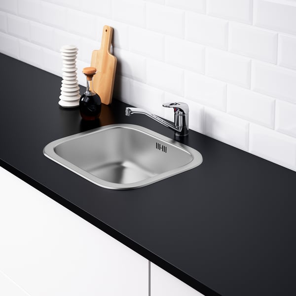 Modern kitchen sink in stainless steel with sound-absorbing material, mounted in black countertop. Chrome tap included.