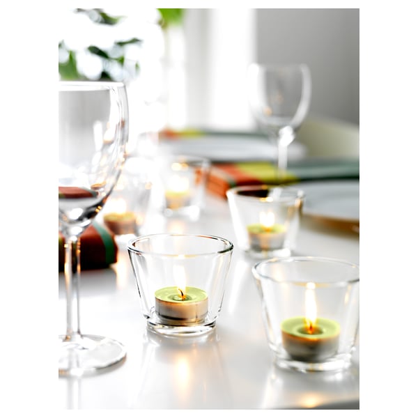 Clear glass tealight holders with green candles on a white table with wine glasses. Elegant and simple.